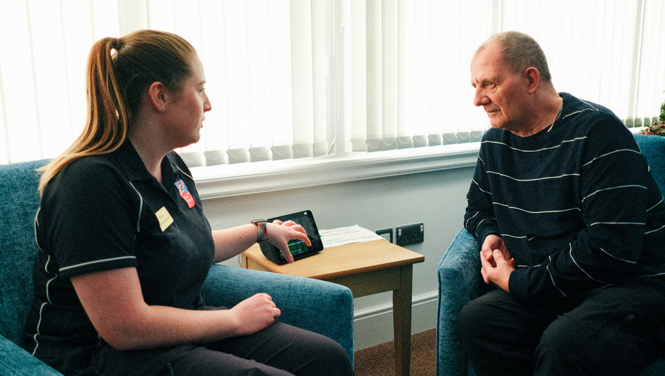 Rhian, a Wellbeing Specialist demonstrates the new Amazon Alexa at the Llandudno Centre to Blind Veteran Jules