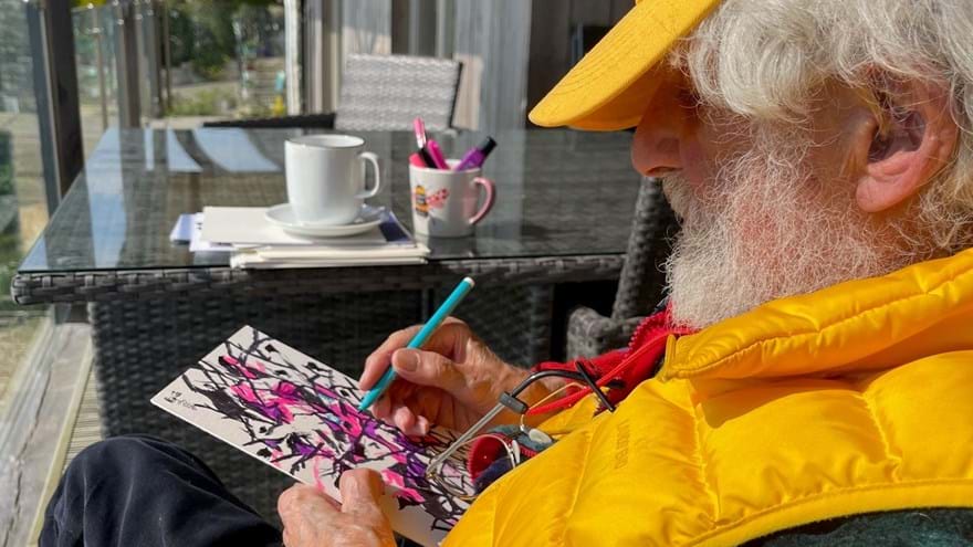 Blind veteran Philip is sitting on a porch and drawing on a piece of card