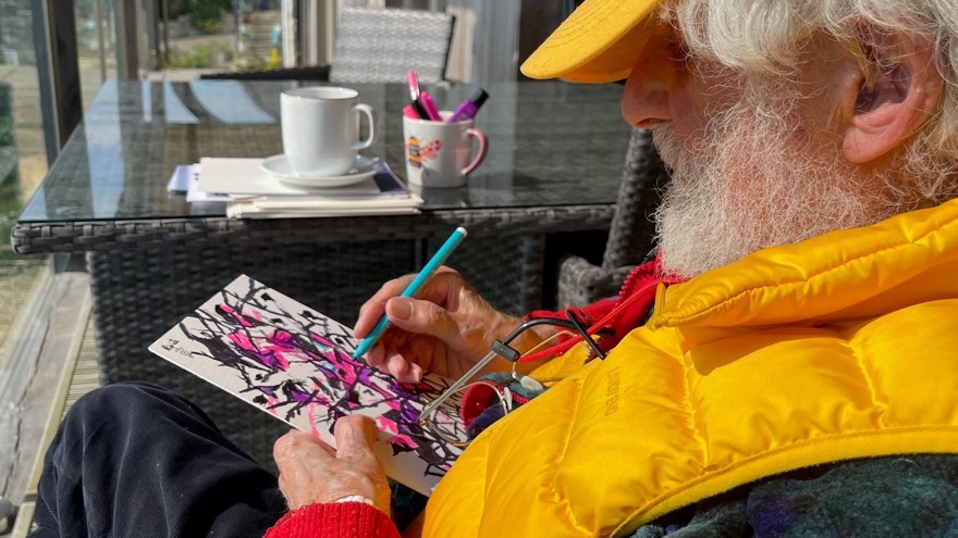 Blind veteran Philip is sitting on a porch and drawing on a piece of card