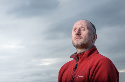 Blind veteran Mark, wearing a red fleece, standing outside on a cloudy grey day