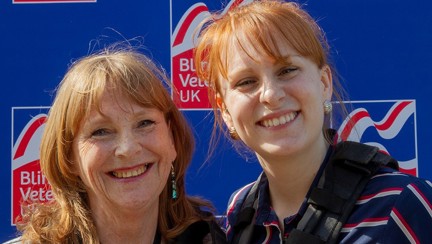 Jennie and Fern are both wearing a harness and standing in front of a Blind Veterans UK branded wall