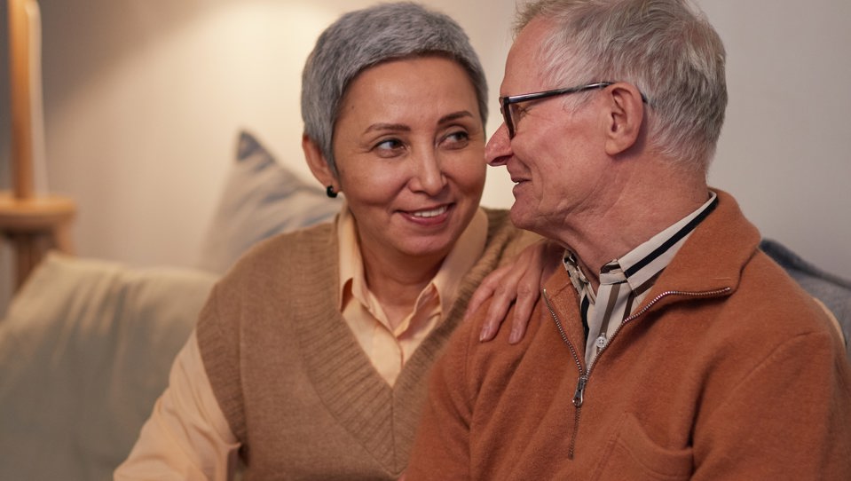 A man and woman sitting on a sofa, holding an ipad, while looking at each other