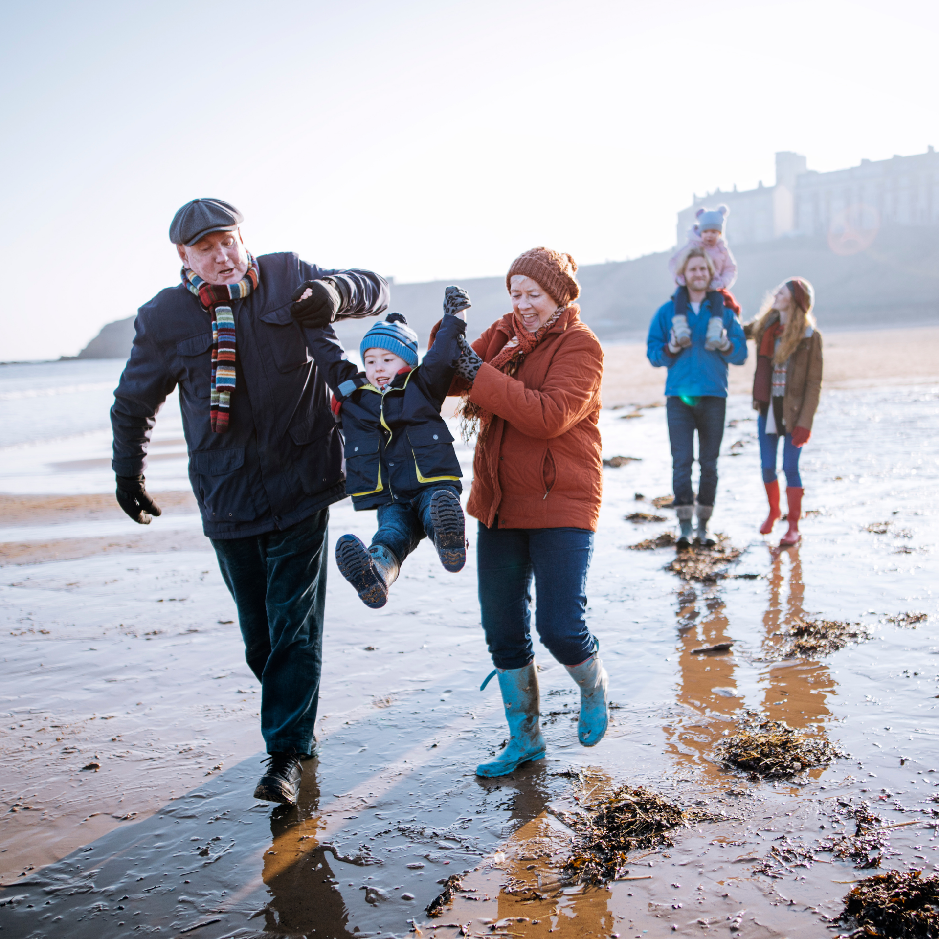 Two happy couples walking along the beach, both with a child in hand