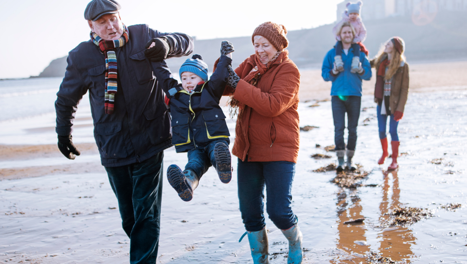 Two happy couples walking along the beach, both with a child in hand