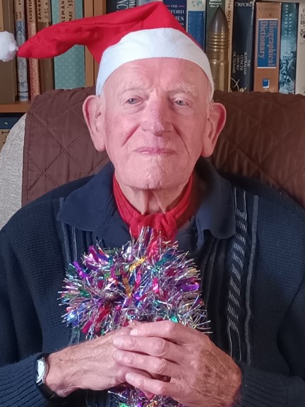 Mike smiling, wearing a Santa hat and holding some colourful tinsel.