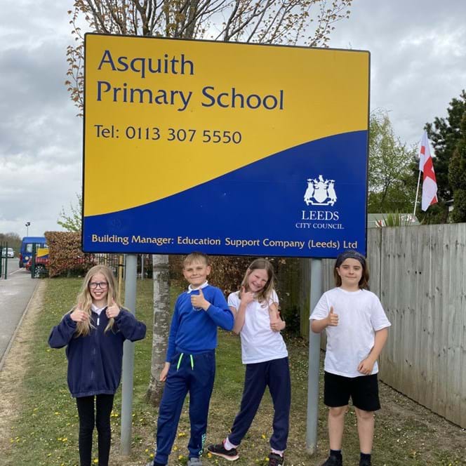 A photo of four primary school children in front of the Asquith Primary School sign