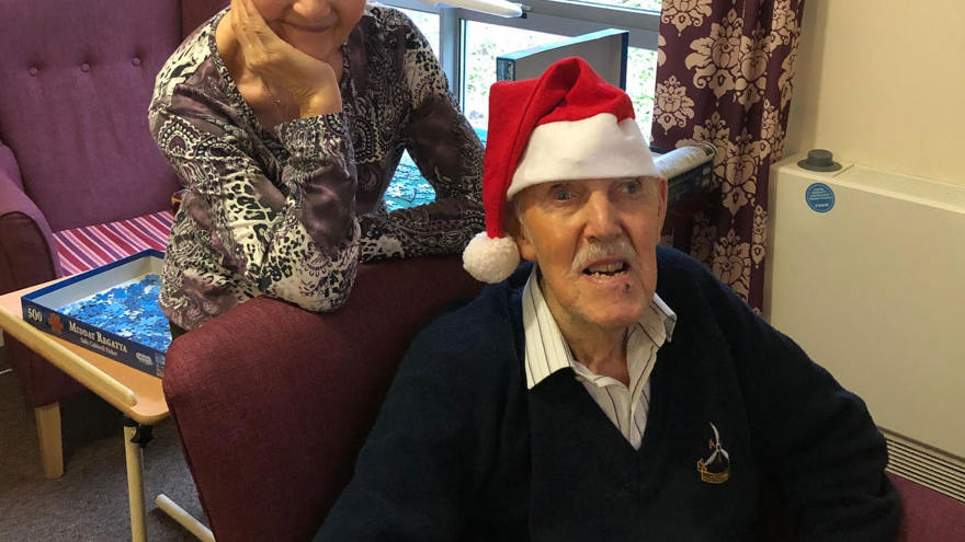 Blind veteran Bill and his wife, smiling and wearing Christmas hats