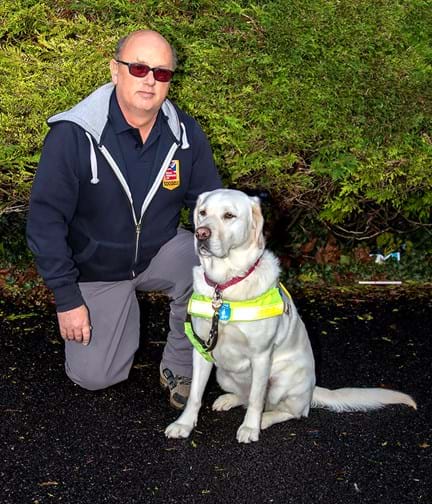 Mark kneeling down next to his guide dog