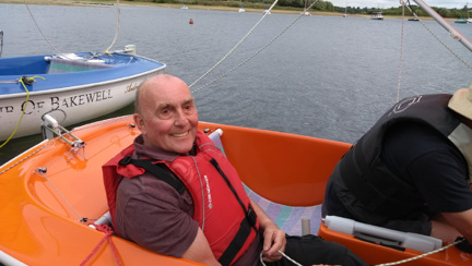 Blind veteran, Simon, smiling as he sits in an orange sailboat on the water