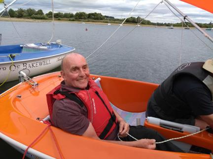 Blind veteran, Simon, smiling as he sits in an orange sailboat on the water