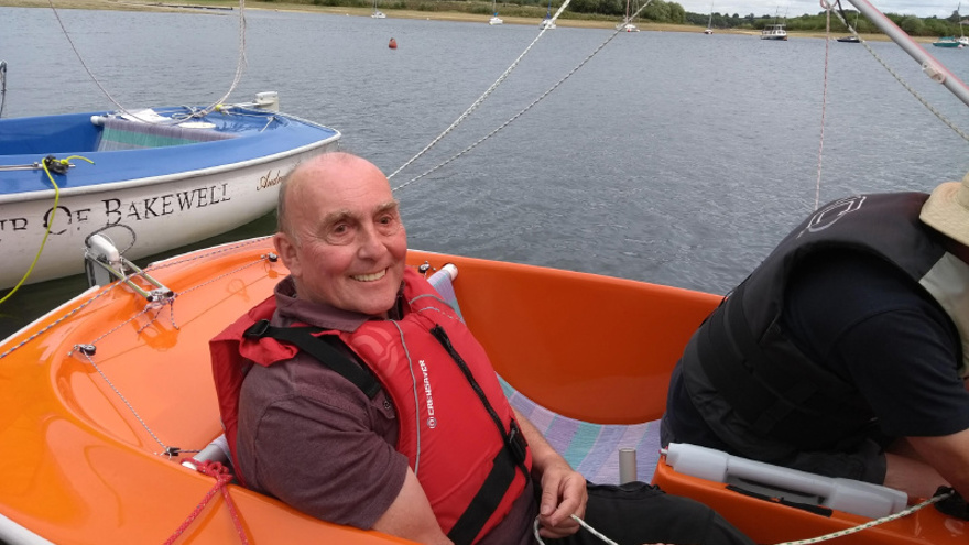 Blind veteran, Simon, smiling as he sits in an orange sailboat on the water