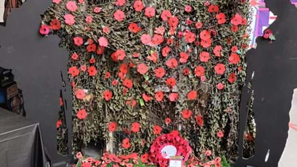 A Blind Veterans UK wreath in front of shower of poppies and two WWI soldier cut outs