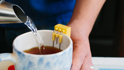 A close up of a hand pouring a cup of tea into a mug which has a liquid level indicator attached.
