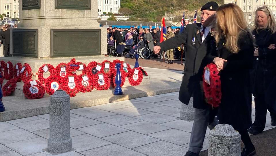 Blind veteran Billy Baxter approaching the Llandudno Town War Memorial to lay a wreath on Remembrance Sunday, accompanied by wreath gifter Kelly of Tom Owens and Sons.