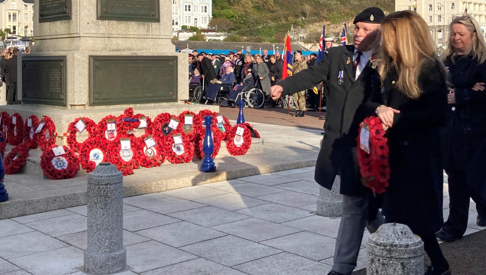 Blind veteran Billy Baxter approaching the Llandudno Town War Memorial to lay a wreath on Remembrance Sunday, accompanied by wreath gifter Kelly of Tom Owens and Sons.