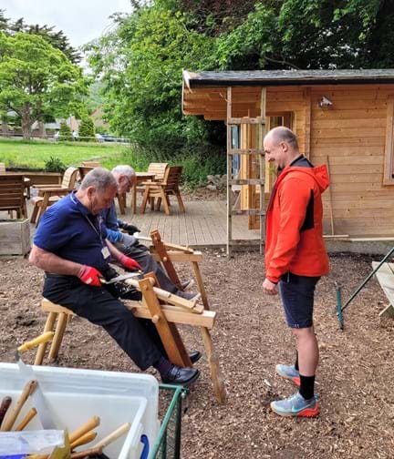 Two blind veterans woodworking, with a wooden cabin in the background