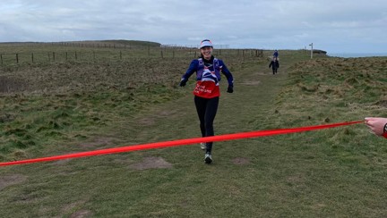 Rachel smiling as she runs towards a red finish line being held by her family