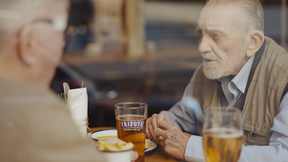 Blind veteran Ken and volunteer Liam sitting down, chatting in a pub, with drinks and food on the table