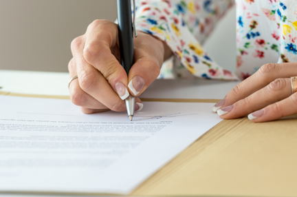 A woman sat at a desk using a pen to write on documents.