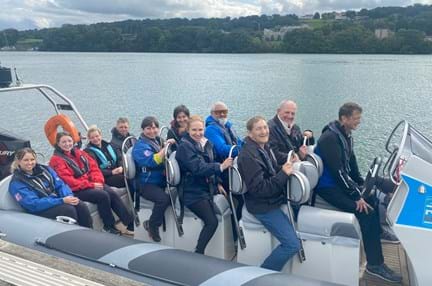 Blind veterans and staff smiling, while sat on a speed boat over a lake