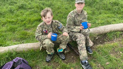 Two boys sat on a log wearing camouflage clothing 