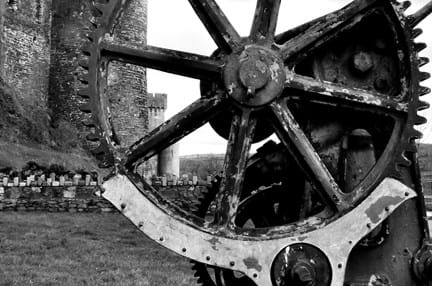 Black and white photograph of a large industrial wheel in front of Conwy Castle