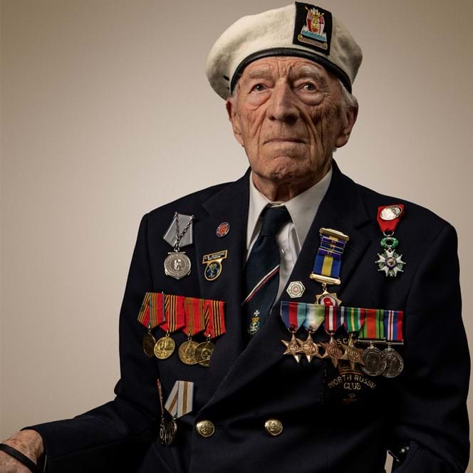 Blind veteran Alec, wearing a suit and his medals sitting in a chain and holding a cane