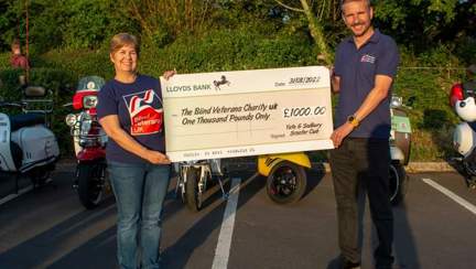 Sally and Colin in their Blind Veterans UK T-shirts holding a giant cheque from the scooter club