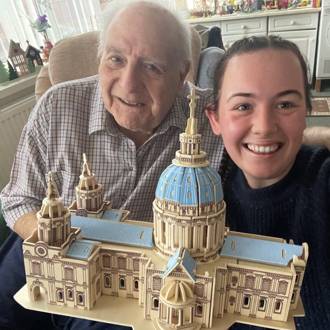 Blind veteran Maurice and volunteer Mia smile and look into camera while holding the cathedral model