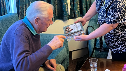 A blind veteran reaching into a box of chocolates as he sits comfortably on a sofa