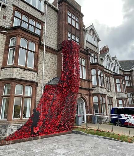 A large poppy blanket, made of up individually knitted poppies, decorating the front entrance of our Llandudno Centre of Wellbeing