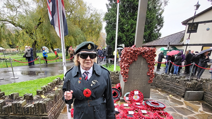 Noeline stood with her white cane in front of the War Memorial with a sea of poppy wreaths at its base