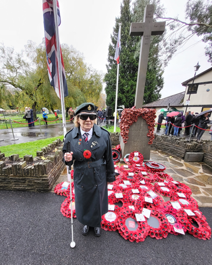 Noeline stood with her white cane in front of the War Memorial with a sea of poppy wreaths at its base