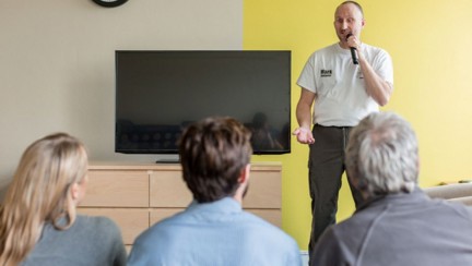 Blind veteran Mark standing in front of a group of people, holding a microphone and talking