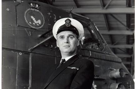 Photo of blind veteran, Terry Bullingham, in his Naval uniform standing in front of a vessel