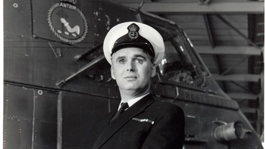 Photo of blind veteran, Terry Bullingham, in his Naval uniform standing in front of a vessel