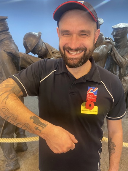 Member of staff wearing Blind Veterans UK t shirt and displaying his tattoo of a soldier with his head bowed down looking at a cross