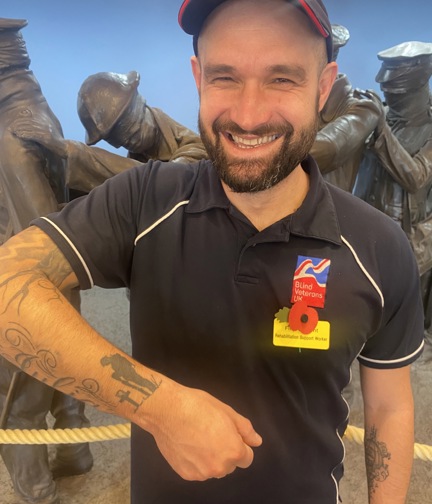 Member of staff wearing Blind Veterans UK t shirt and displaying his tattoo of a soldier with his head bowed down looking at a cross