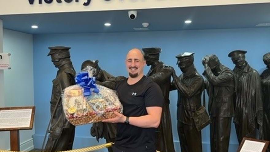Adam holding his hamper of treats at our Centre of Wellbeing in Llandudno standing in front of the Victory over Blindness statue