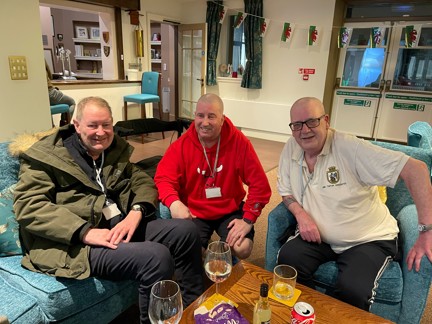 Left to right, Stuart, John, and Jim pictured smiling and sitting down on a sofa and chairs together