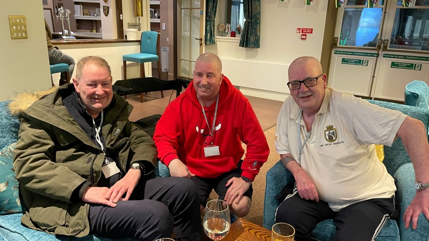 Left to right, Stuart, John, and Jim pictured smiling and sitting down on a sofa and chairs together