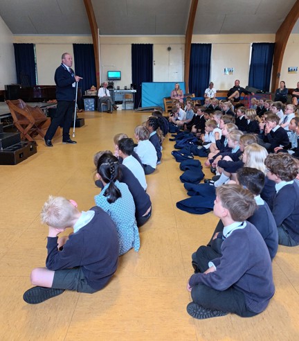 Blind veteran Billy standing in front of a group of pupils and teachers giving a talk in a school hall