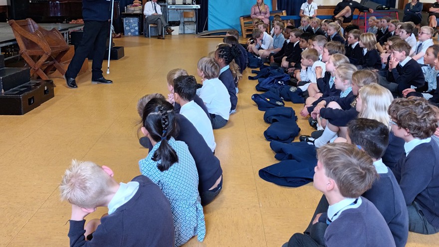 Blind veteran Billy standing in front of a group of pupils and teachers giving a talk in a school hall