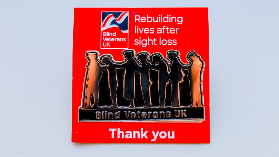 A Blind Veterans UK pin badge of the Victory Over Blindness "Lads" statue, pinned to branded packaging