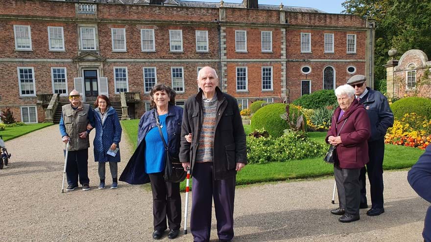 Blind veterans enjoying their day out to Erddig in North Wales - The group stand in front of a grand house in the gardens