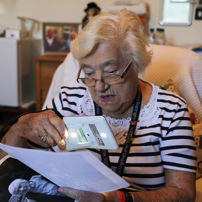 A photo of blind veteran Win Amos using OrCam glasses to read letters and look at old photos