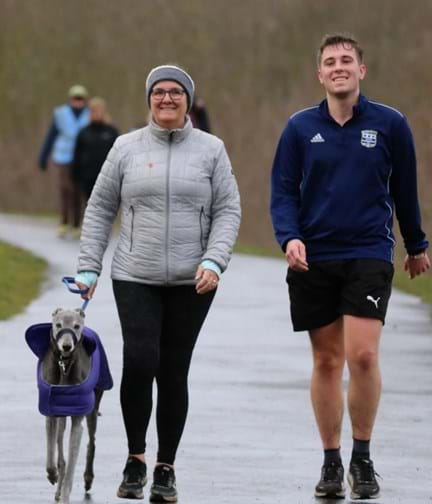 Alison walking in the rain along a tarmac path with her Son Ryan and her dog