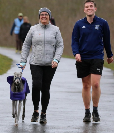 Alison walking in the rain along a tarmac path with her Son Ryan and her dog