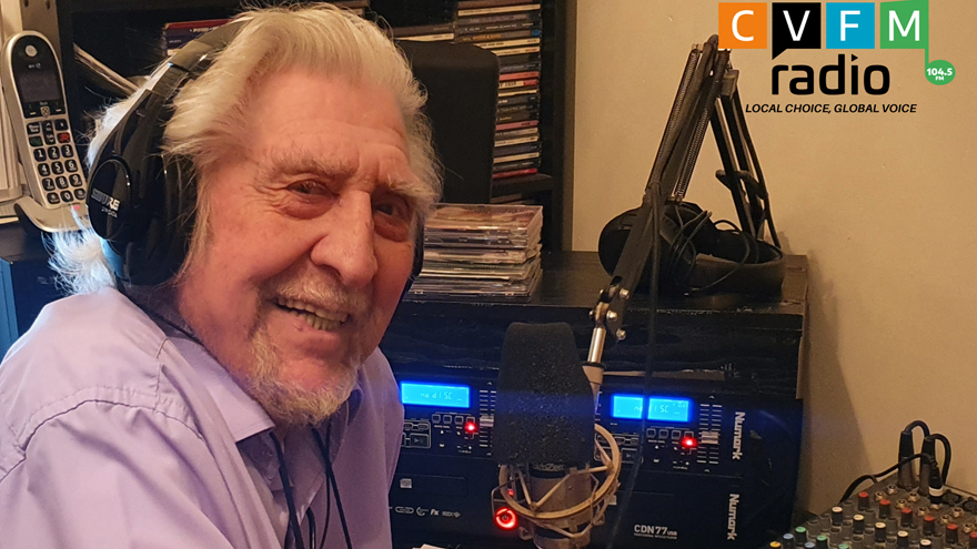 A photo of blind veteran Sam, pictured smiling, wearing headphones while and speaking into a microphone while hosting his radio show