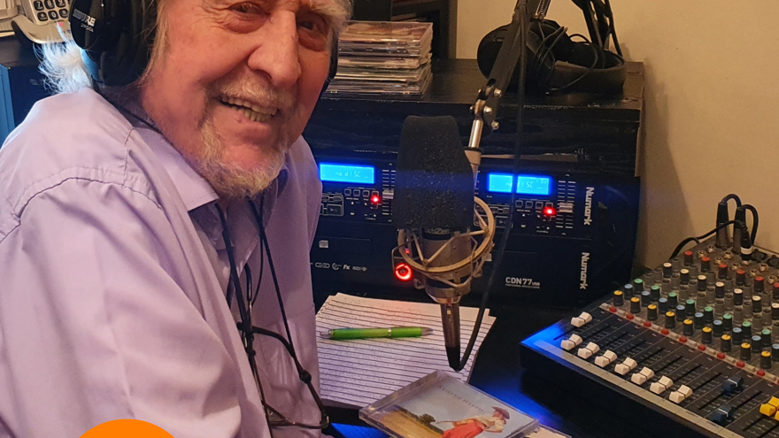 A photo of blind veteran Sam, pictured smiling, wearing headphones while and speaking into a microphone while hosting his radio show